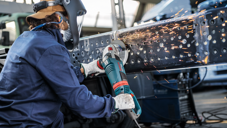 PRO Metal Grinding Disc, A 24 S BF, 180 x 6.6 x 22.23 mm, Depressed Centre Person wearing safety equipment grinds a metal beam, generating bright sparks.
