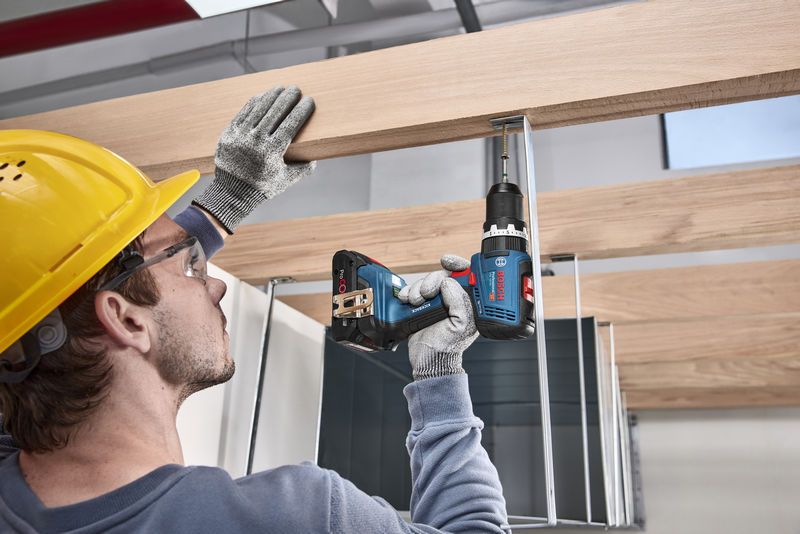 A person wearing safety equipment drills a screw into a wooden beam.