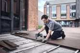A person wearing safety equipment installs decking boards using a cordless drill.