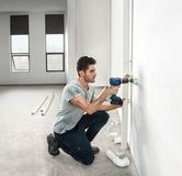 A person drills into a wall to install piping in a bright, unfinished room.