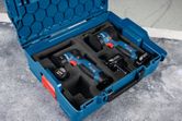 Cordless power tools and batteries organized in a blue carrying case on a work surface.