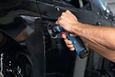 A person uses a random orbit sander to polish a car door surface.