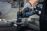 A person wearing safety equipment uses a random orbit sander to polish a car surface.