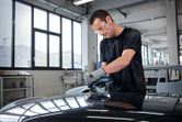 Person wearing safety equipment sanding a car roof with a random orbit sander.