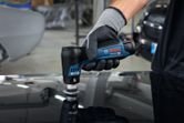 Person wearing safety equipment uses a cordless sander to polish a car surface.