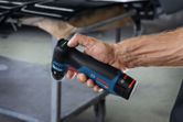 A person holds a cordless random orbit sander in a workshop setting.