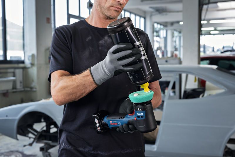 A person wearing safety equipment applies polish to a polisher in an auto workshop.