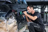 A person wearing safety equipment polishes a car door with a cordless tool.