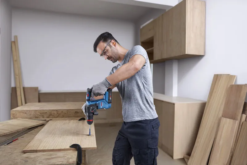 GBH 18V-18 X A person wearing safety equipment drills into wood using a cordless rotary hammer.