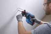 A person wearing safety equipment drills into a wall with a rotary hammer.