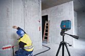 A person wearing safety equipment marks a wall using a laser leveling tool.