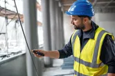 A person wearing safety equipment tests a cable with a non-contact voltage tester.