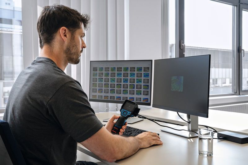A person reviews thermal images on dual monitors using a thermo camera at a desk.