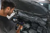 A person inspects a car engine using a handheld thermo camera.
