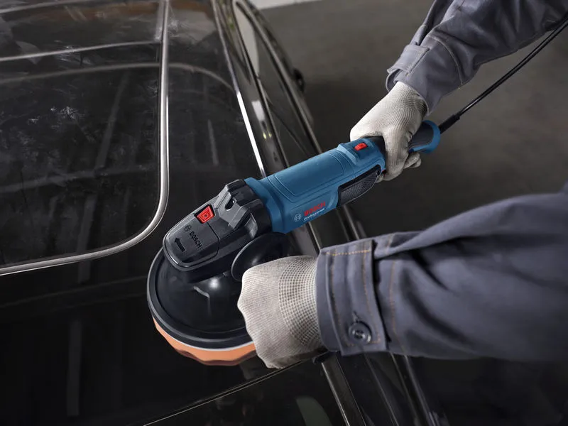 A person wearing safety equipment polishes a car roof with a power polisher.