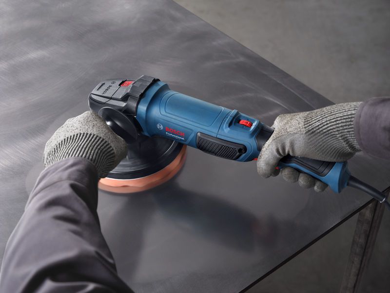 A person wearing safety equipment uses a polisher on a metal surface.
