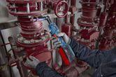 A person wearing safety equipment tightens a pipe bolt with a cordless ratchet wrench.