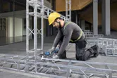 A person wearing safety equipment tightens bolts on a metal frame with a cordless ratchet wrench.