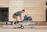 A person wearing safety equipment moves a saw stand with a mounted table saw.