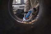 A person wearing safety equipment grinds the inside of a large metal pipe with a straight grinder.