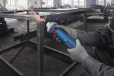A person wearing safety equipment uses a straight grinder to smooth a metal frame.