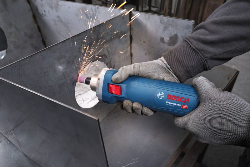 A person wearing safety equipment grinds metal with a straight grinder, creating sparks.