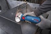A person wearing safety equipment grinds metal with a straight grinder, creating sparks.