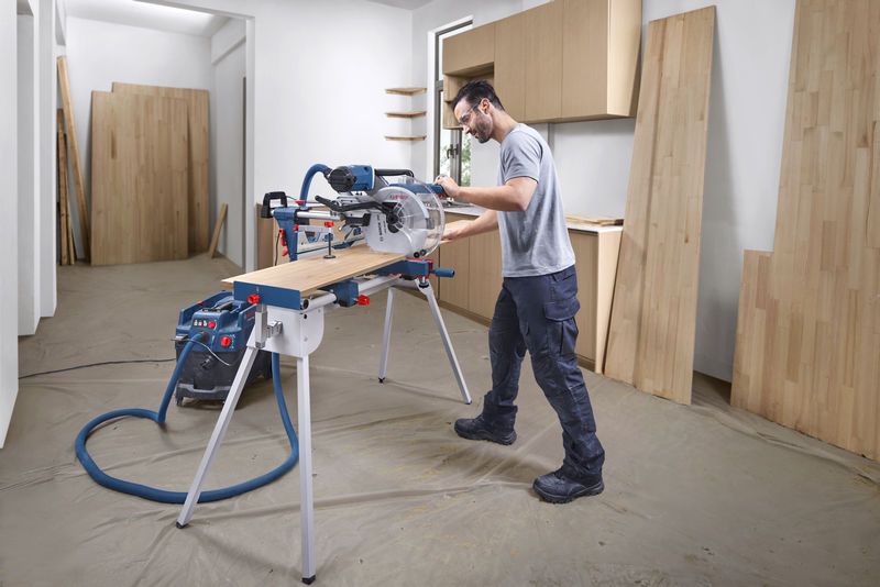 GCM 340-305 D A person wearing safety equipment cuts a wooden board using a mitre saw in a workshop.