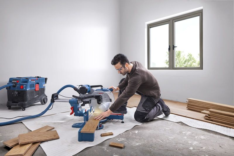 GCM 340-305 D A person wearing safety equipment cuts wood planks with a mitre saw in a bright room.