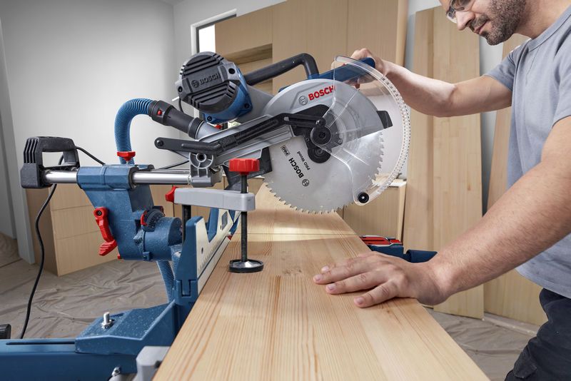 GCM 340-305 D A person operates a mitre saw to cut a wooden board in a workshop.