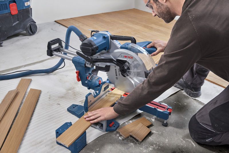 GCM 340-305 D A person wearing safety equipment cuts wooden flooring with a sliding mitre saw.