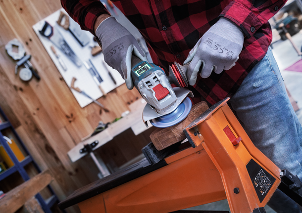 EXPERT Multi Material Carbide Grinding Head Medium, Flat, X-LOCK, 115 mm, 22.23 mm Person wearing safety equipment uses an angle grinder to sand wood clamped to a workbench.