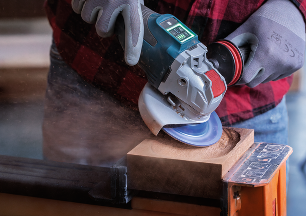 EXPERT Multi Material Carbide Grinding Head Medium, Flat, X-LOCK, 115 mm, 22.23 mm Worker wearing safety equipment uses an angle grinder to carve a circular hole in wood.