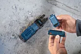Person replacing a battery in a power tool base on a dusty concrete floor.