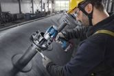 A person wearing safety equipment tightens bolts on industrial piping with a cordless impact wrench.