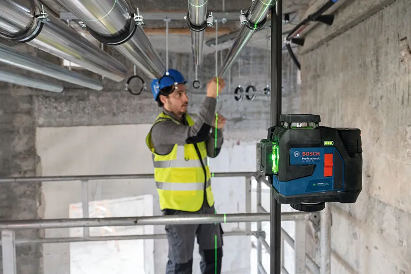 A person wearing safety equipment aligns pipes using a laser leveling tool.