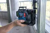 Person holds a laser leveling tool against a metal stud in a construction area.