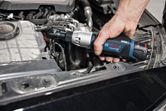 A person uses a cordless ratchet wrench to tighten a bolt in a car engine.