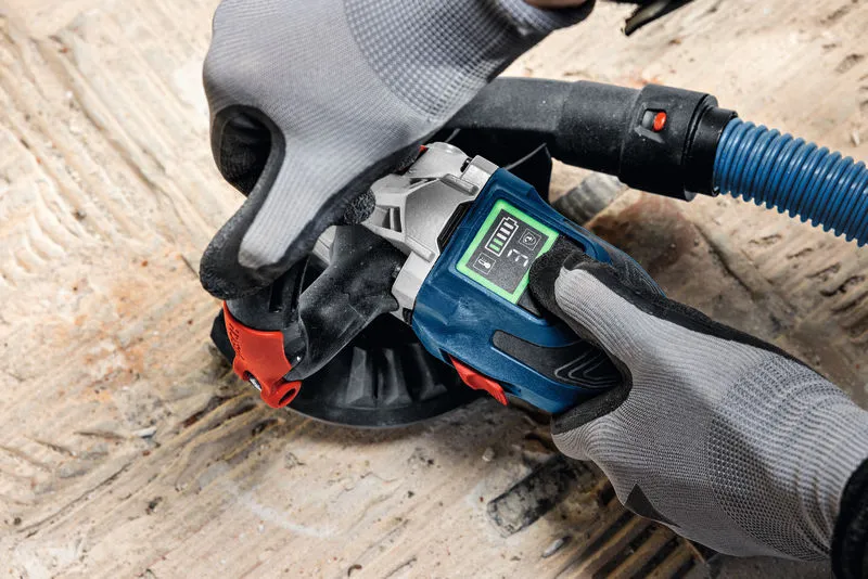 A person wearing safety equipment operates a concrete grinder on a rough floor surface.