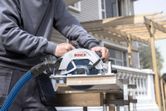 A person uses a cordless circular saw to cut wood outdoors.