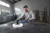 A person wearing safety equipment uses a polisher on a large metal surface.