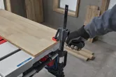 A person wearing safety equipment clamps a wooden board to a table saw.