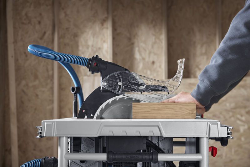 A person guides wood through a table saw with dust extraction in a workshop.