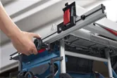 Person adjusts a portable table saw fence using a large black adjustment knob.