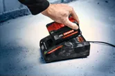 A person places a red and black battery pack onto a charging station.