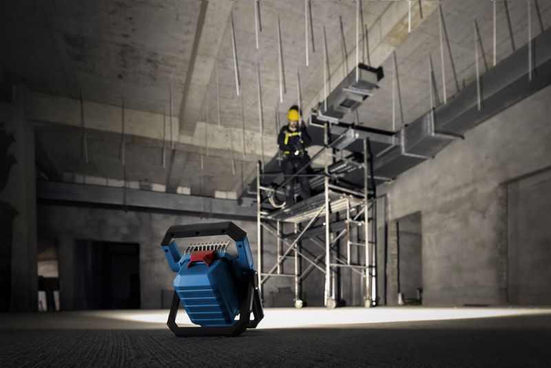 Cordless jobsite light illuminating a person wearing safety equipment on scaffolding.