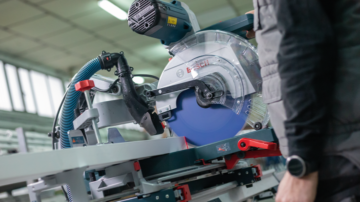 Object #200585100: 7557700_app_web_01 Person wearing safety equipment operates a circular saw in a workshop.