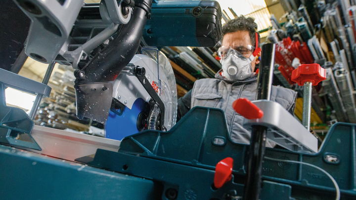 Object #200585104: 7557700_app_web_05 Person wearing safety equipment operates a circular saw in an industrial workspace.