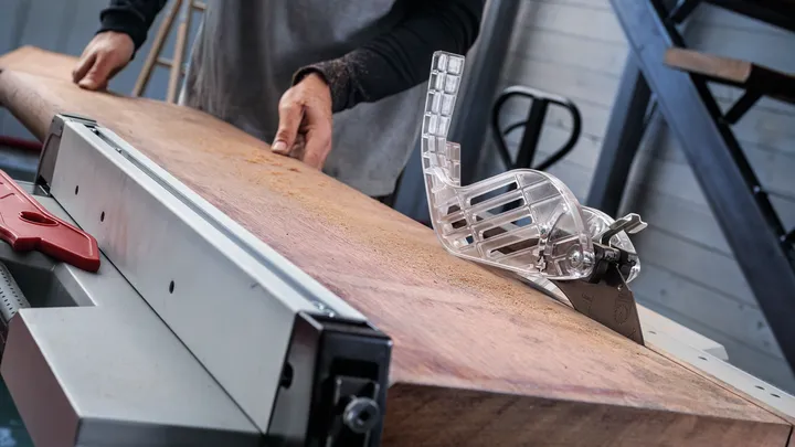 Object #200585343: 7557712_app_web_08 Person pushing a large wooden board through a table saw in a workshop.