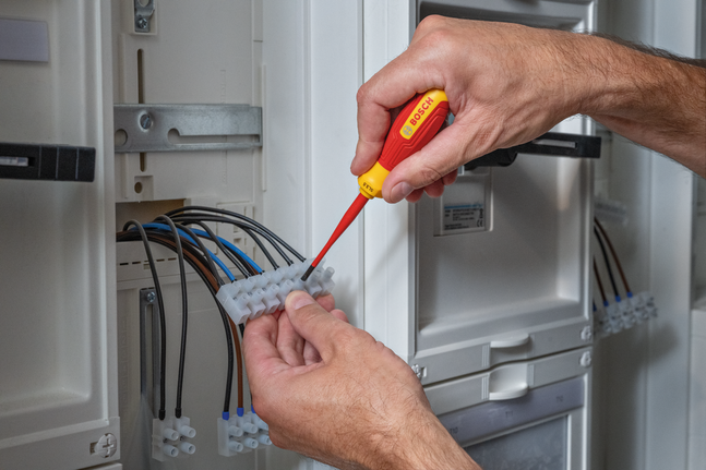 Person tightens electrical connections inside a circuit panel using an insulated screwdriver.